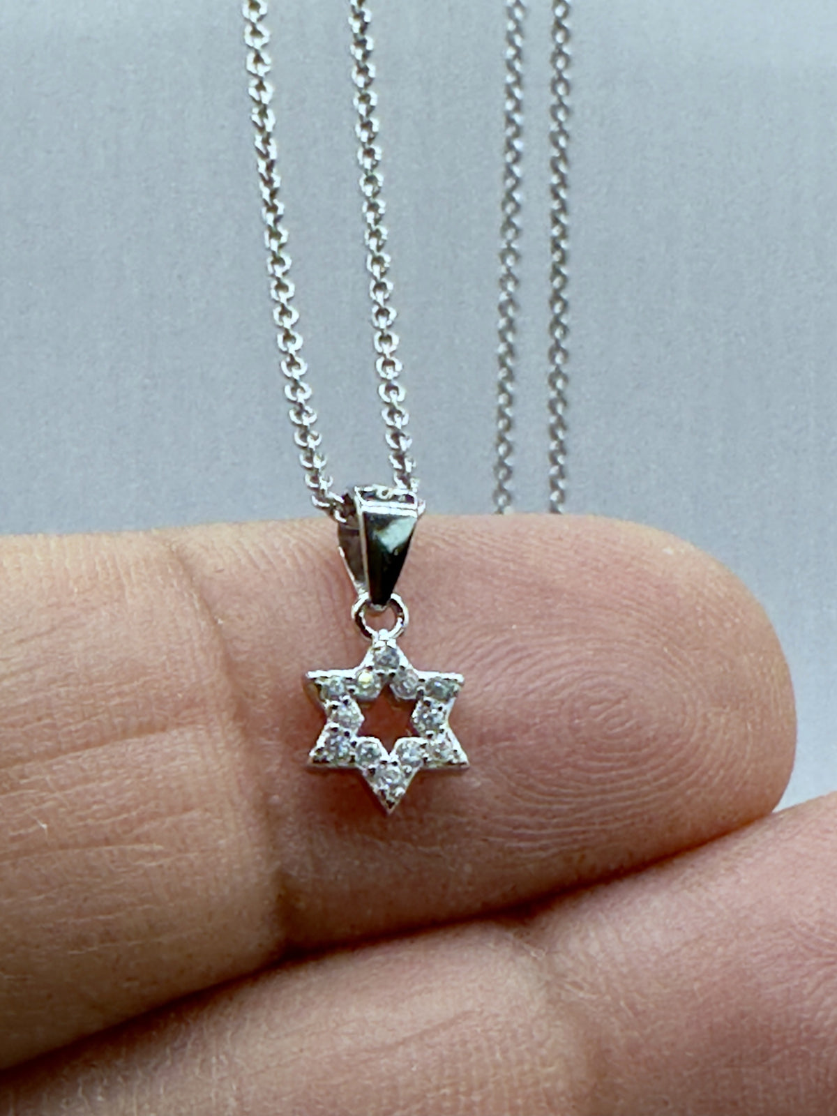 Dainty pavé Star of David pendant on a fingertip for scale