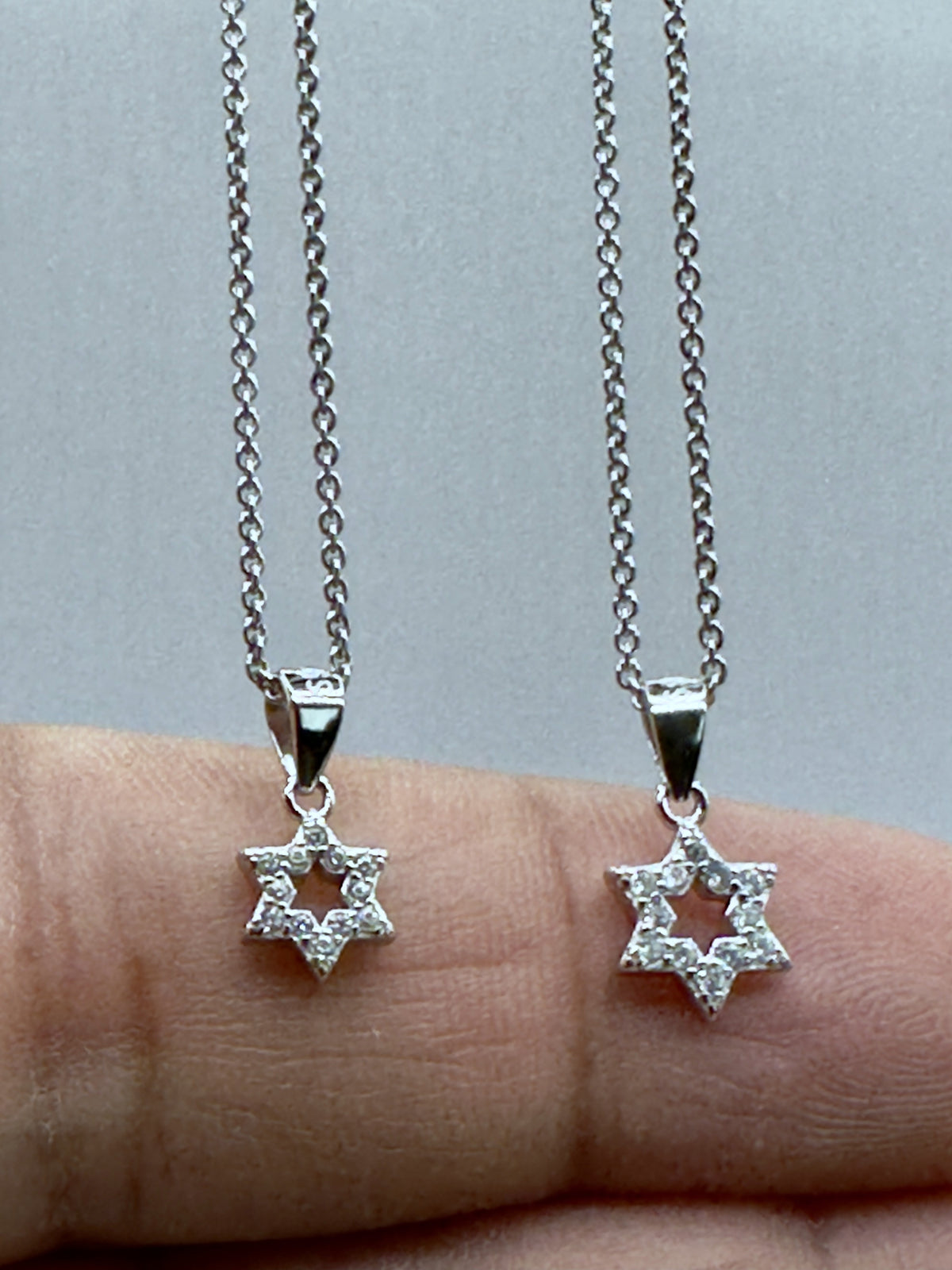 Small and large pavé Star of David pendants compared on a hand